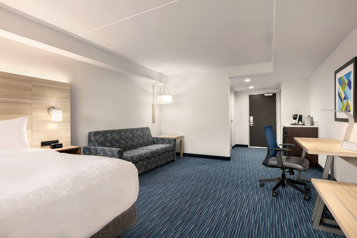 A hotel room with a large bed, a sofa, a desk, and a chair.