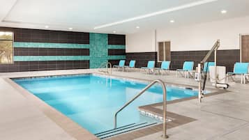 An indoor swimming pool with multiple lanes, a changing room area, and a seating area with chairs.