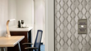 A room with a patterned wallpaper, a sign indicating a room for handicapped individuals, a desk with a lamp, and a chair.