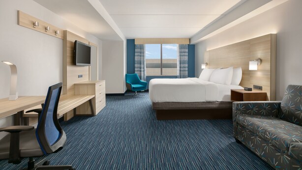 A hotel room with a bed, a desk, a chair, a TV, and a window with curtains.