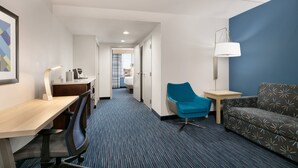 A hotel room with a desk, chair, sofa, and a lamp.