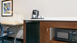 A kitchenette with a coffee maker, microwave, and a framed abstract painting on the wall.