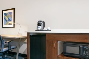 Eine Küchenzeile mit Kaffeemaschine, Mikrowelle und einem gerahmten abstrakten Gemälde an der Wand.