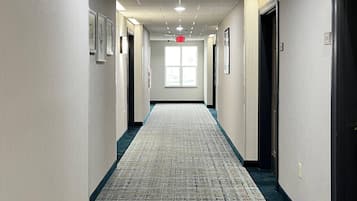 Een hotelgang met vloerbedekking, kunstwerken in lijsten aan de muren, en deuren aan beide kanten.