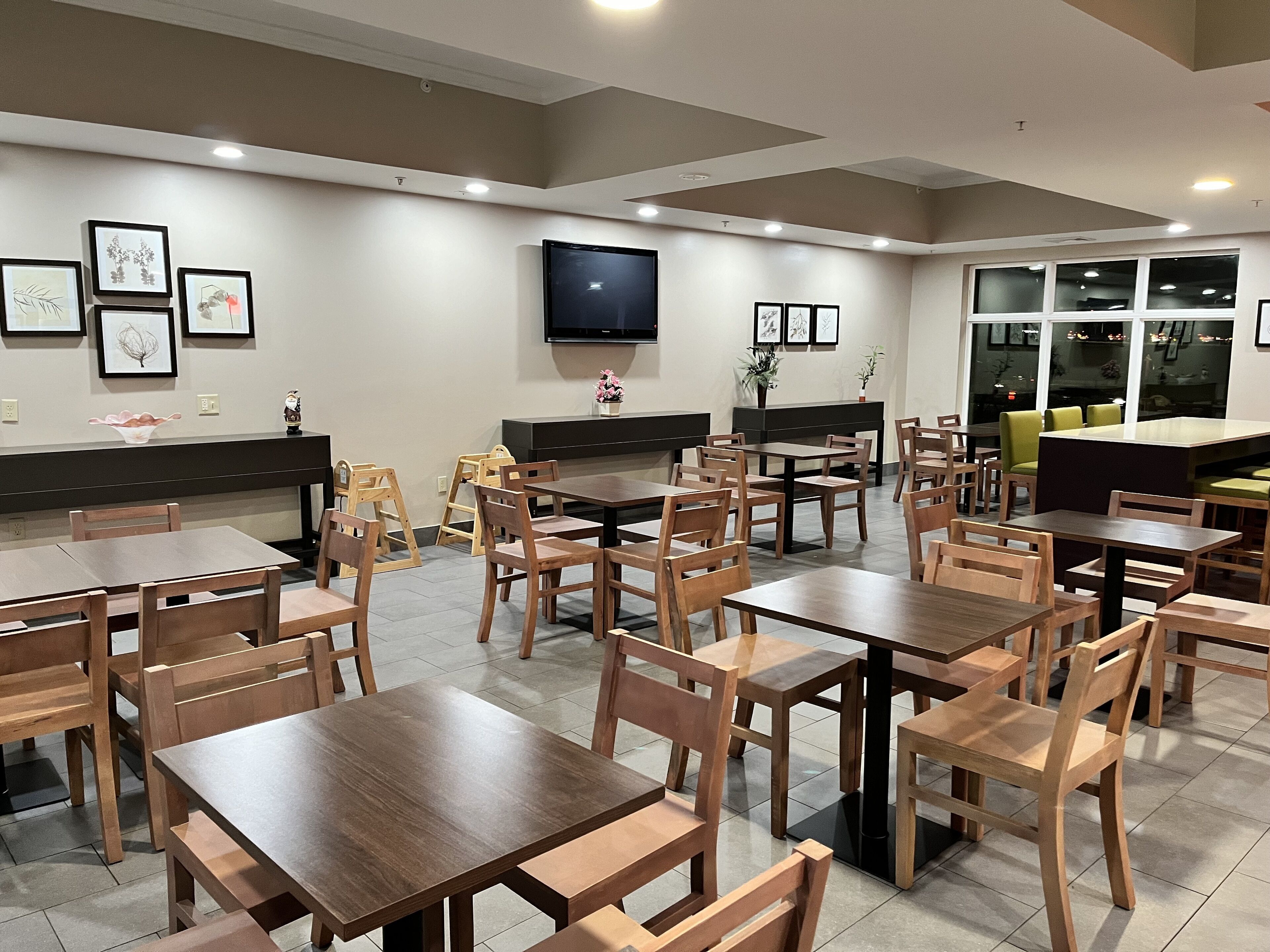 Un restaurant avec des tables et des chaises en bois, un téléviseur à écran plat fixé au mur et des œuvres d’art encadrées qui décorent les murs.