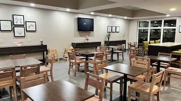Un restaurant avec des tables et des chaises en bois, un téléviseur à écran plat fixé au mur et des œuvres d’art encadrées qui décorent les murs.