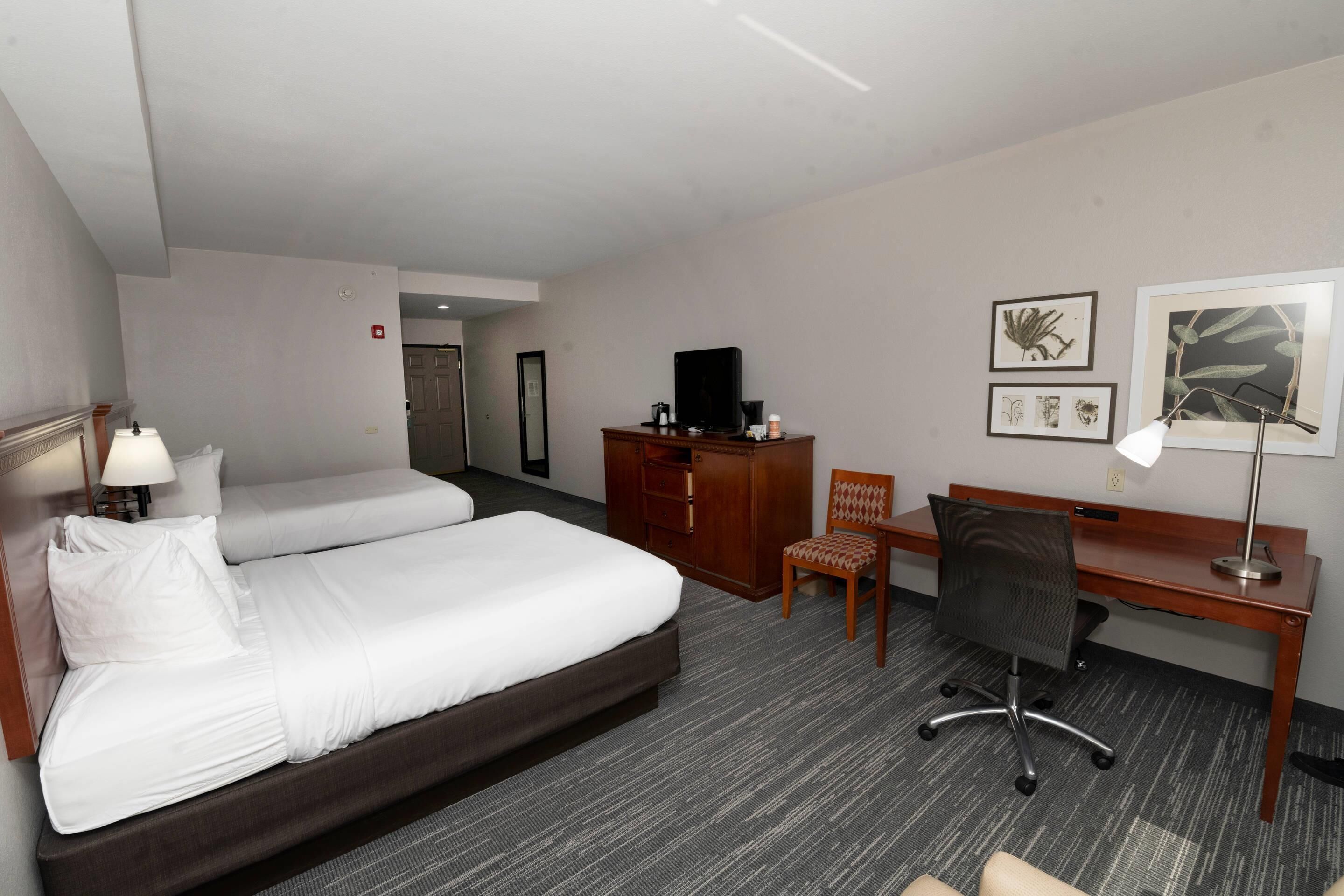 Habitación de hotel con dos camas, un escritorio, una silla, un televisor y cuadros en la pared.