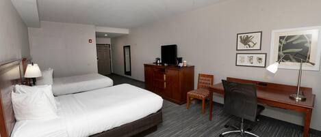 Une chambre d’hôtel avec deux lits, un bureau, une chaise, une télévision et des œuvres d’art encadrées au mur.