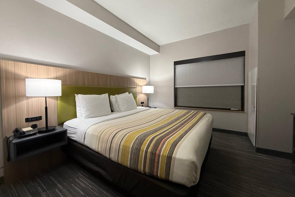 A hotel room with a bed, two bedside lamps, a telephone, a window with blinds, and a headboard.