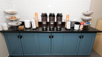 A kitchen area with a blue cabinet, a coffee station with branded dispensers, and various food items on shelves.