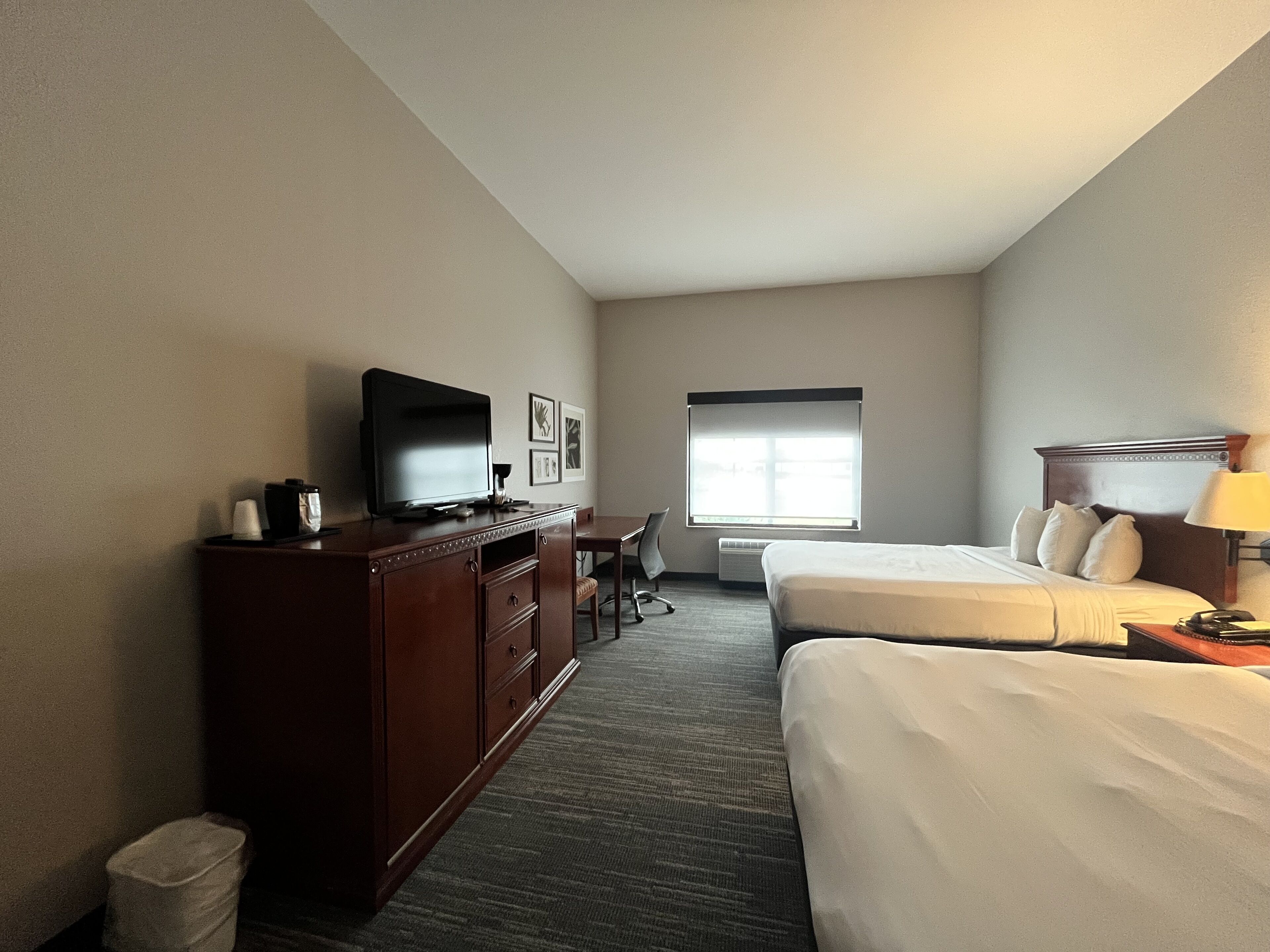 A hotel room with a bed, a desk with a chair, a television, and a window.