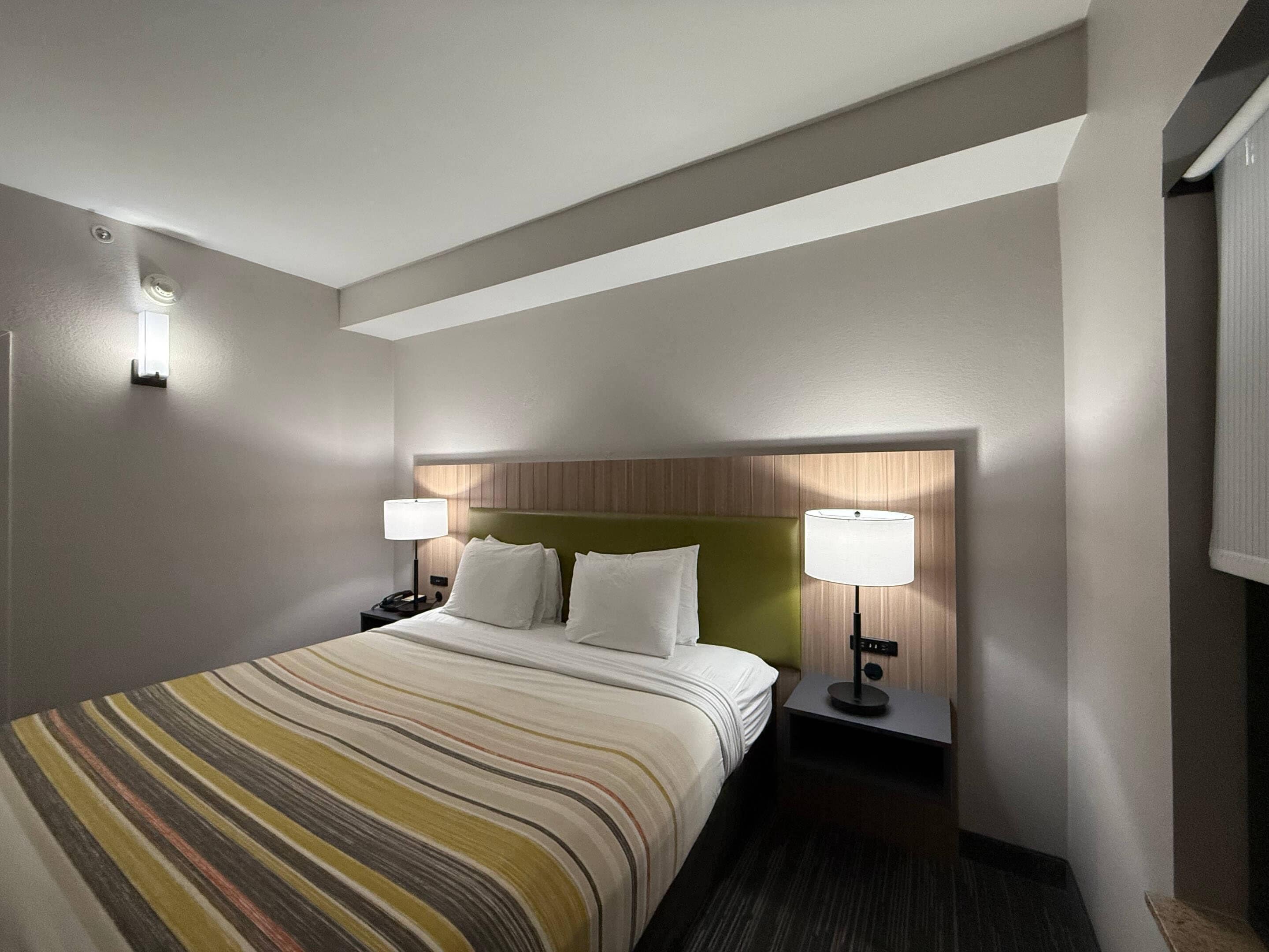 A hotel room with a bed, two bedside tables, a headboard, and wall-mounted lamps.