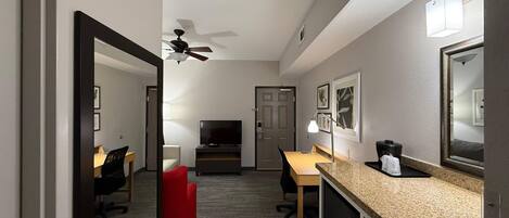 A hotel room with a desk, chair, television, ceiling fan, and a large mirror.