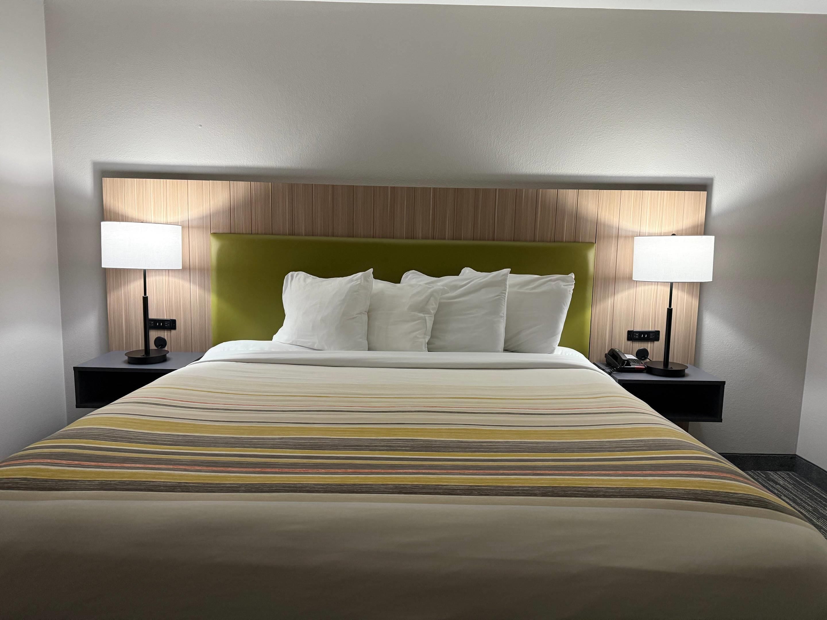 Hotellihuone, jossa on sänky, kaksi yöpöytää valaisimineen, vihreä pääty ja raidallinen päiväpeite.