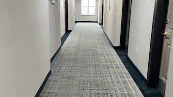 A hotel hallway with a patterned carpet, doors on both sides, and framed pictures on the walls.