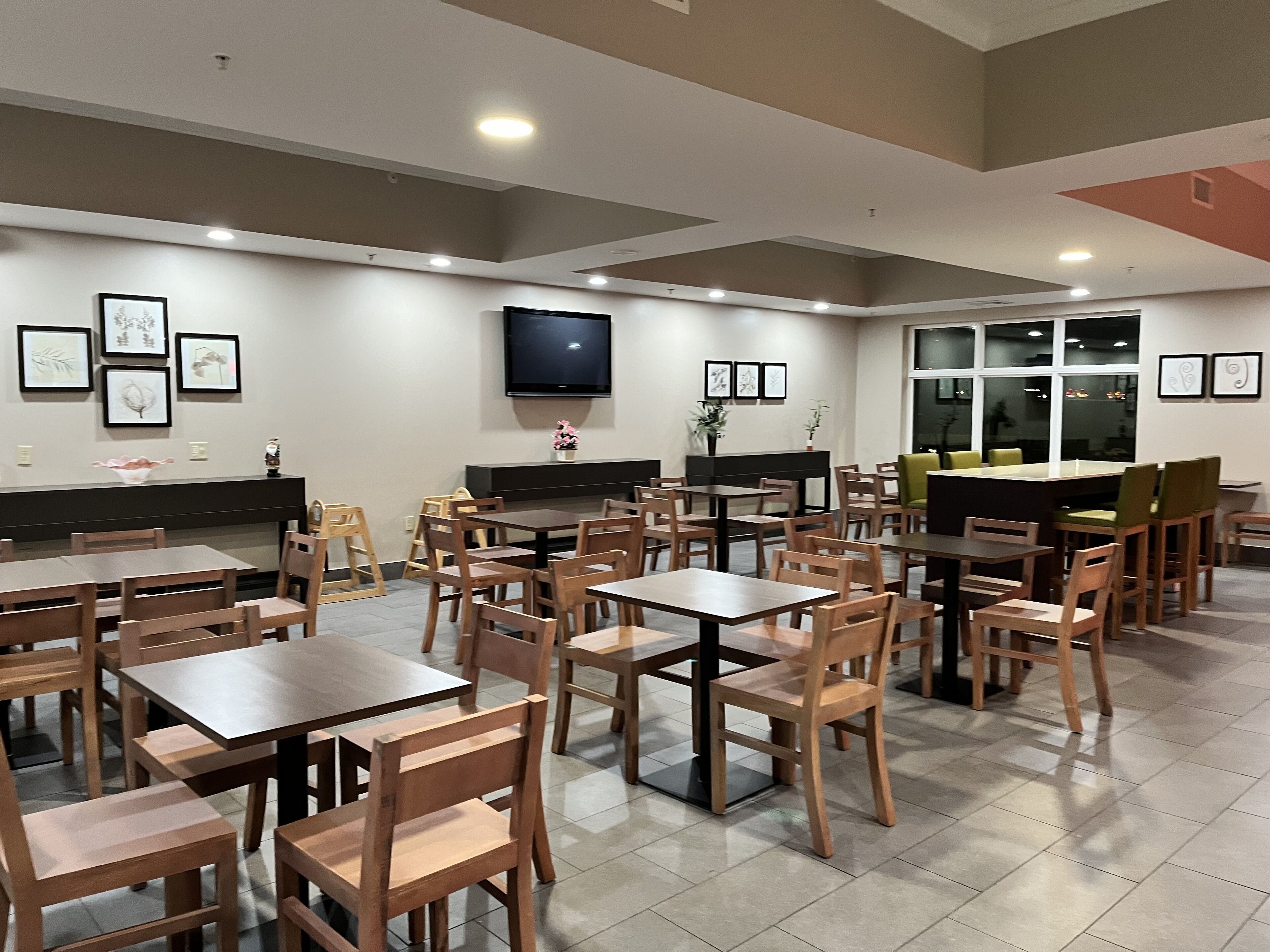 Un restaurant spacieux, doté de nombreuses tables et chaises, d’un téléviseur à écran plat fixé au mur et d’œuvres d’art encadrées qui décorent les murs.