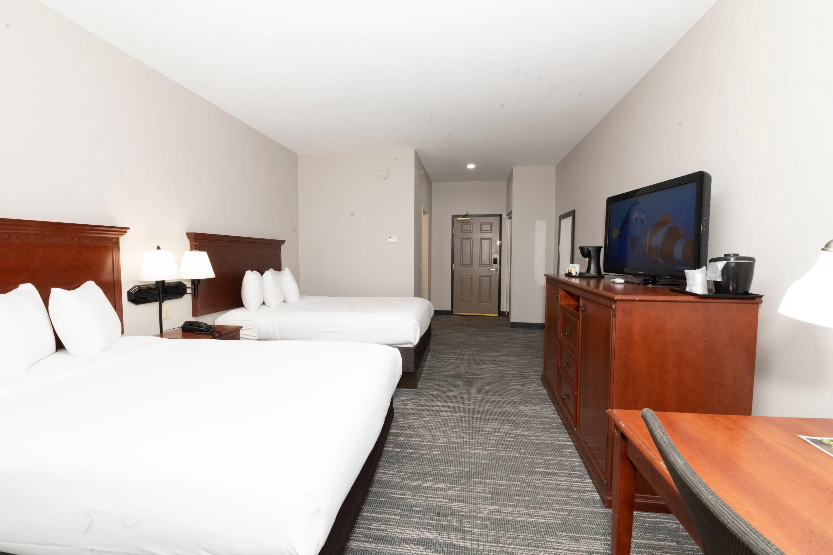 A hotel room with two beds, a television, a desk, and a chair.