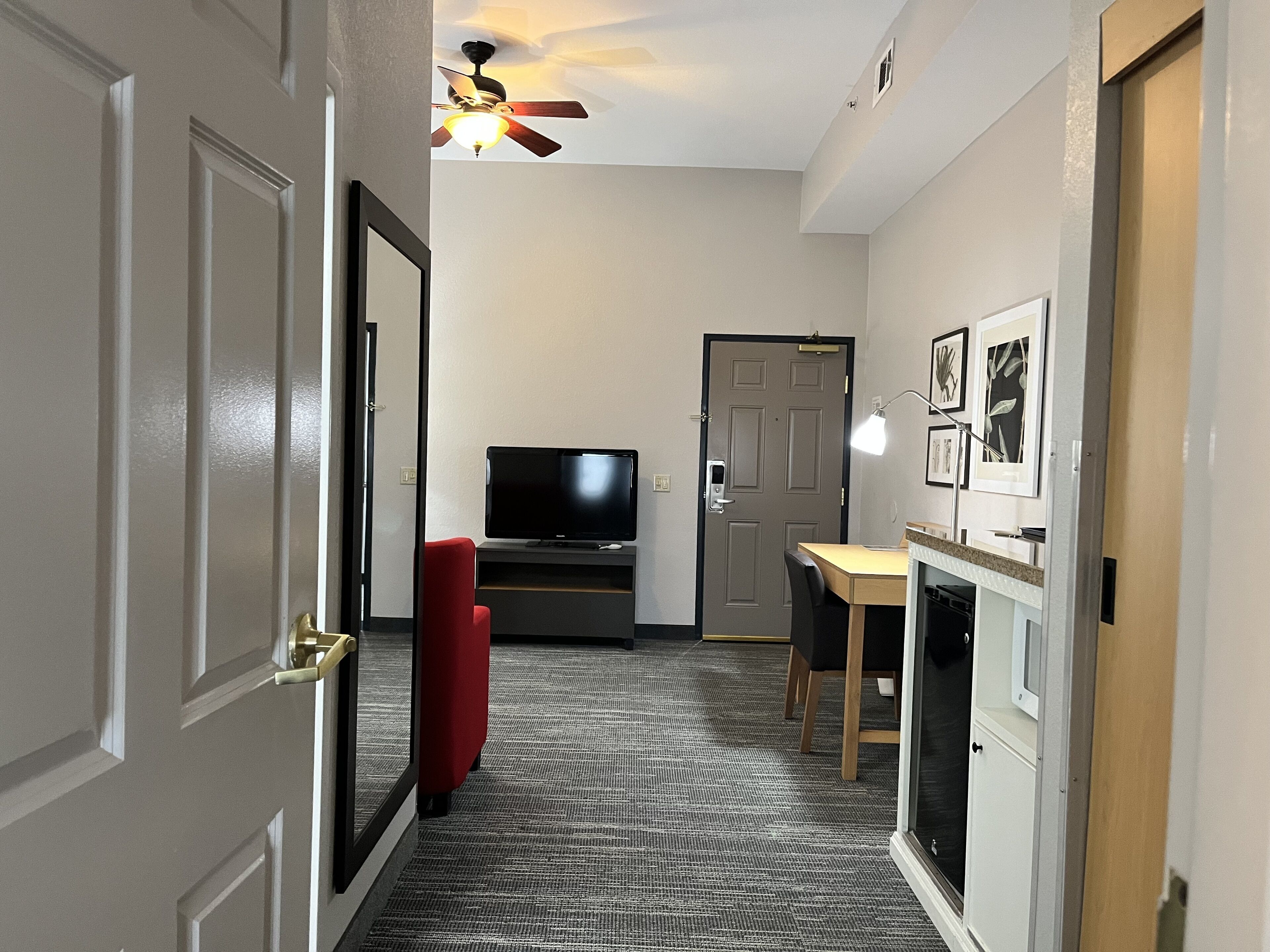 A hallway with a ceiling fan, a television, a red chair, and a small table with a lamp.