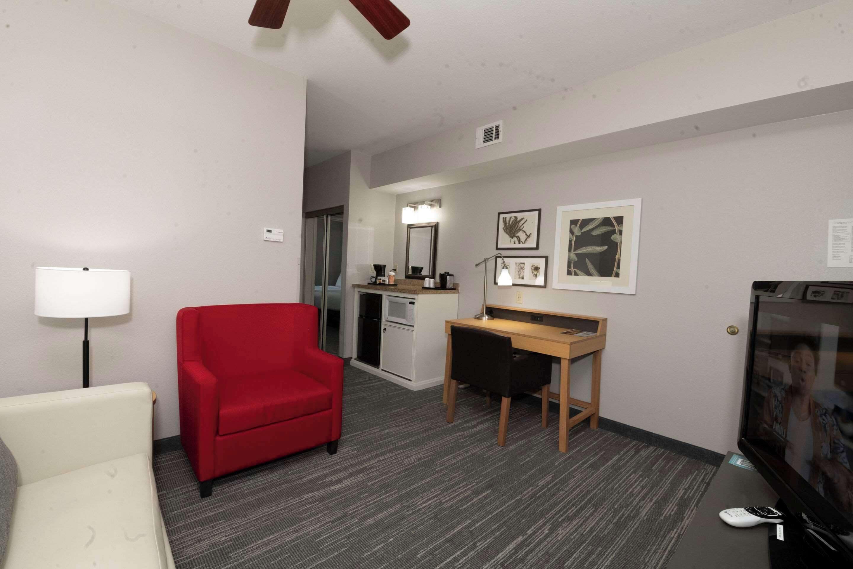 Una habitación de hotel con un sillón rojo, un escritorio, un televisor y una kitchenette pequeña.