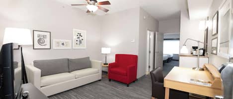 Ein Hotelzimmer mit einer Couch, einem roten Sessel, einem Schreibtisch und einem Deckenventilator.