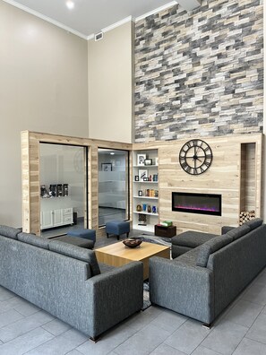 A modern living room with grey sofas, a wooden coffee table, and a stone-patterned wall. - Country Inn & Suites by Radisson, Harrisburg - Hershey West, PA (Harrisburg)