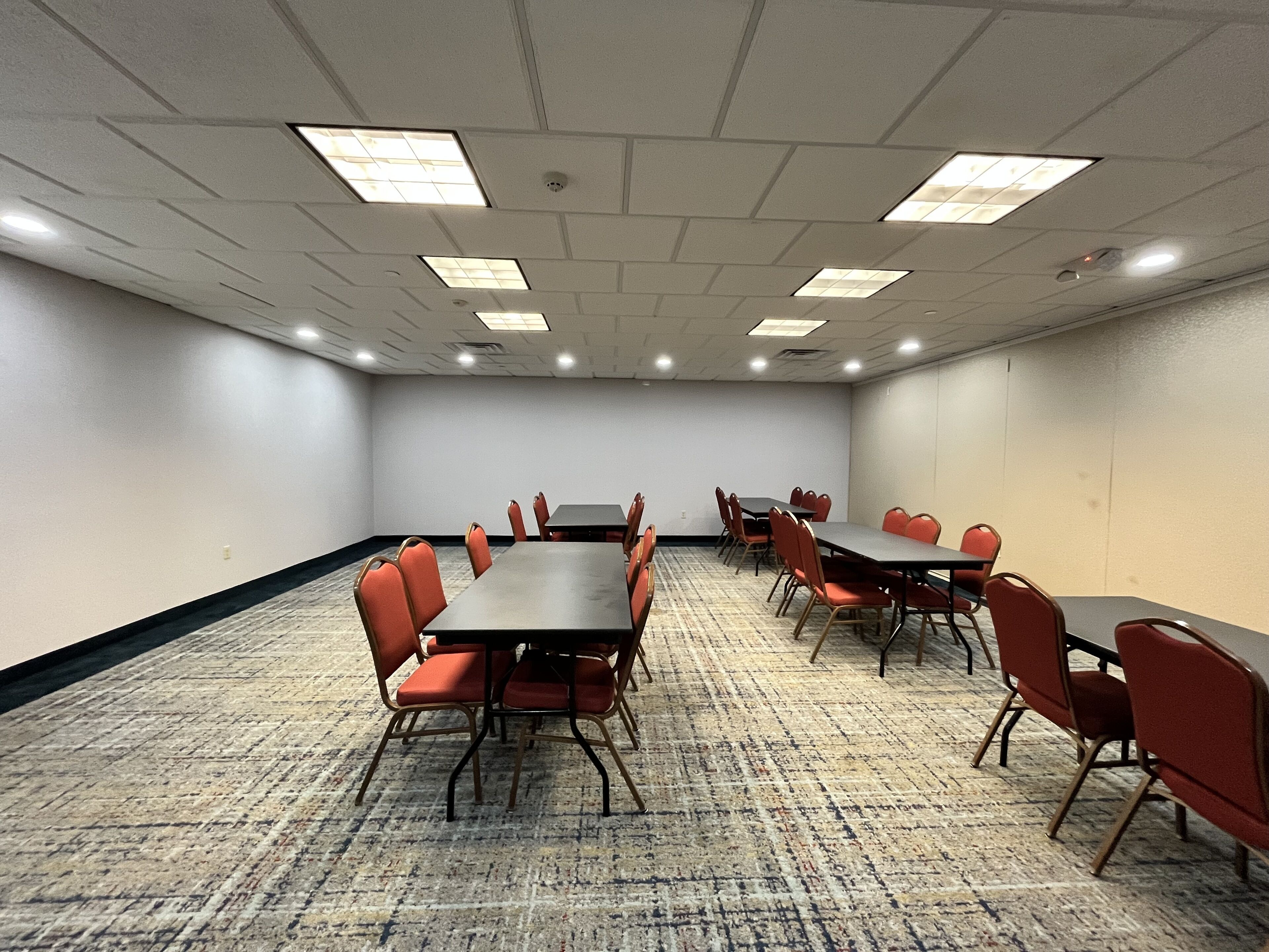 A conference room with a carpeted floor, multiple tables and chairs, and ceiling lights.