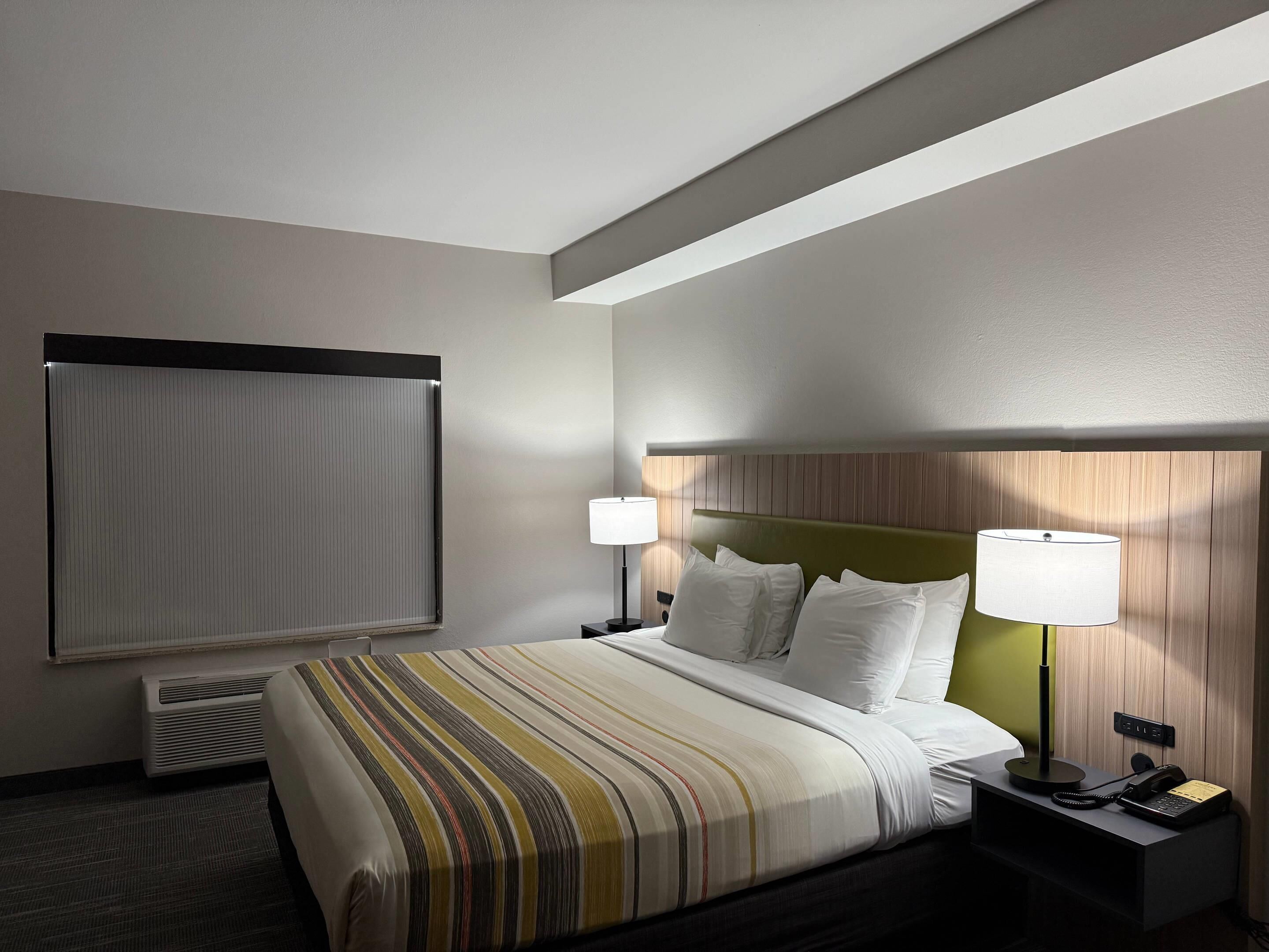 A hotel room with a bed, two bedside lamps, a telephone, and a window with blinds.