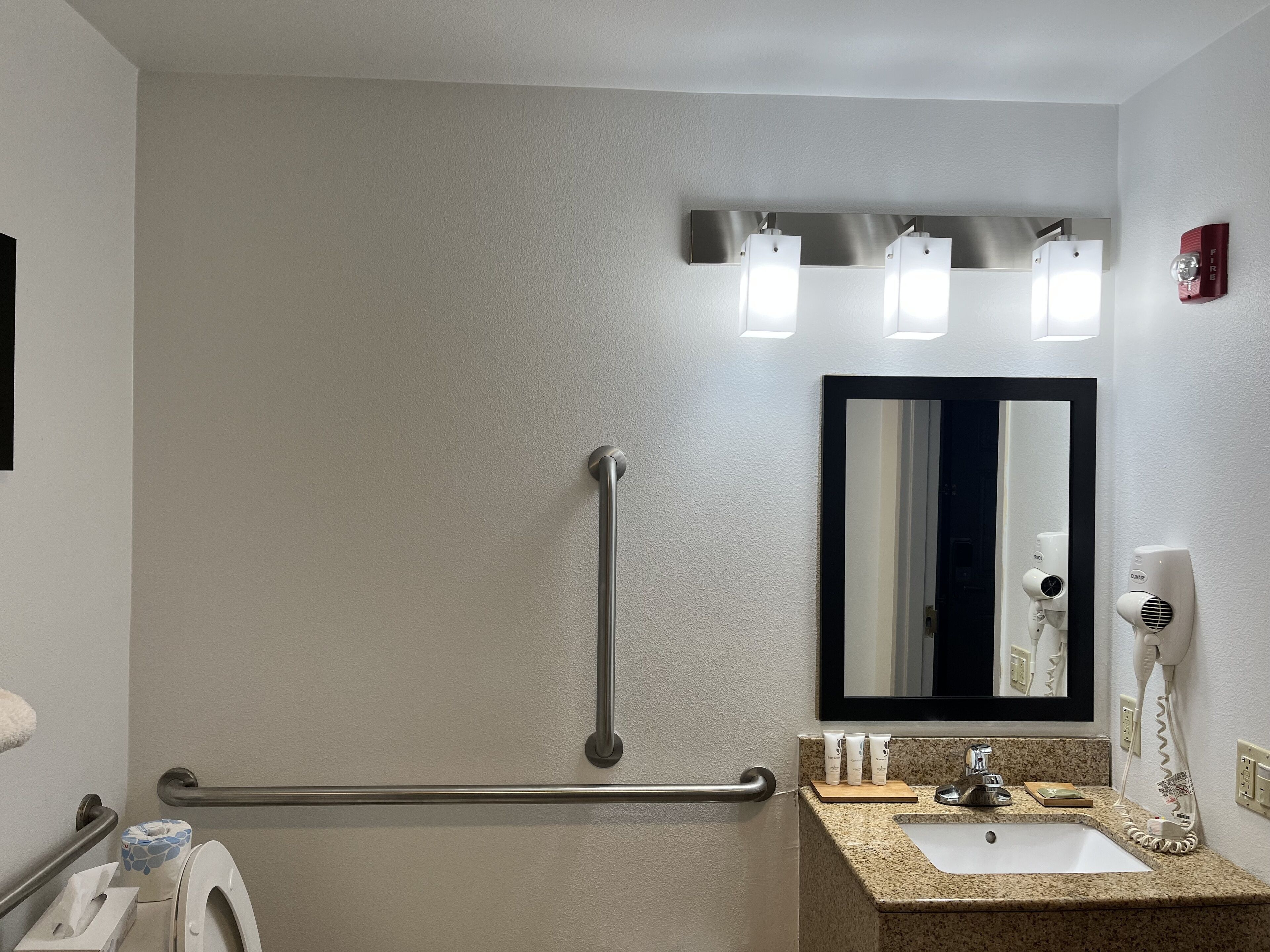 A bathroom with a handrail, a sink, a mirror, and a hairdryer.