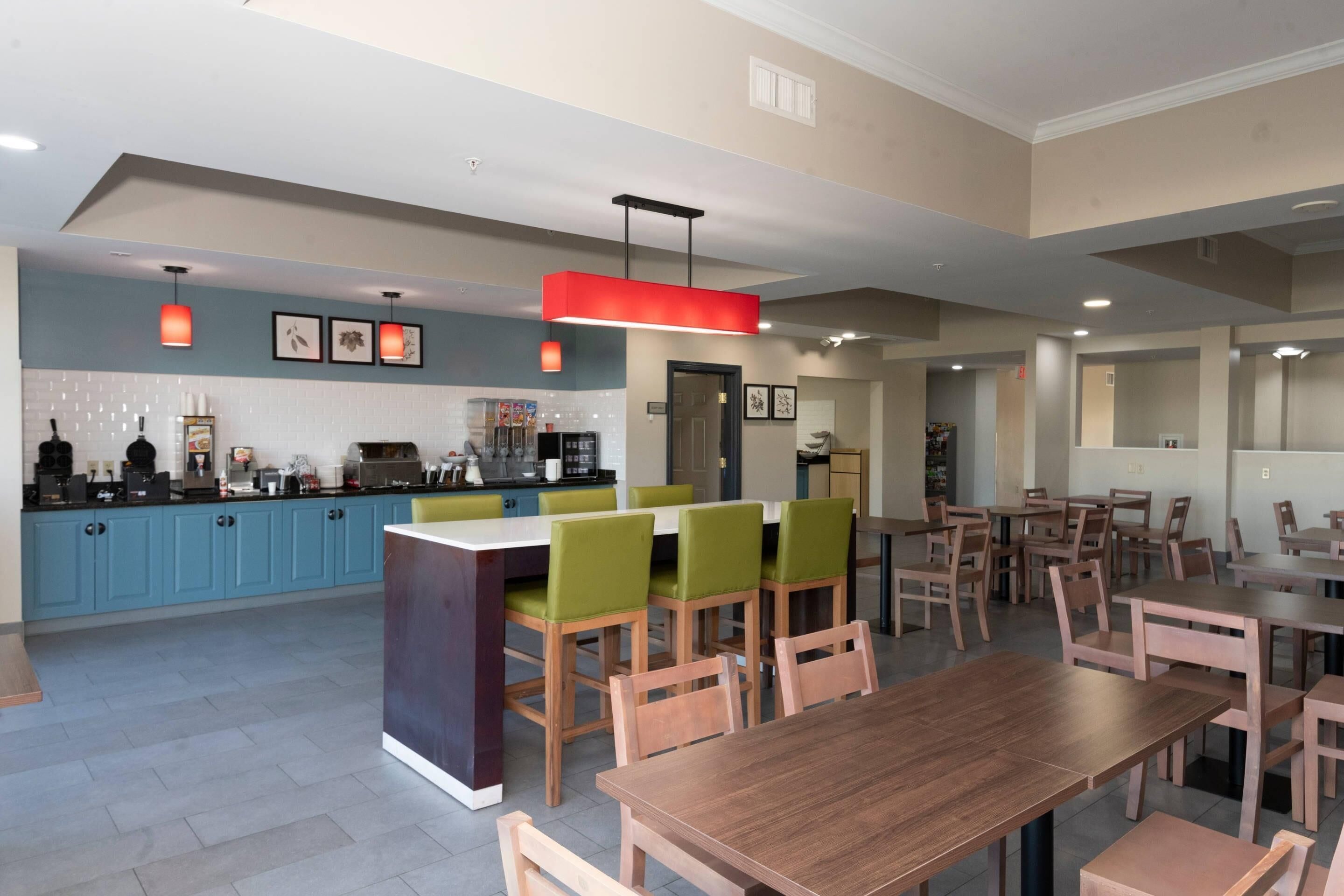A modern dining area with wooden tables and chairs, a central island with seating, and a kitchen area in the background.