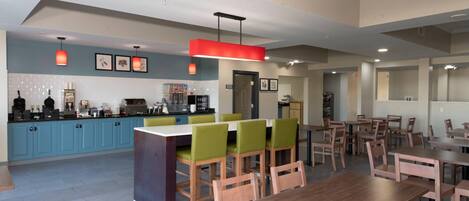 A modern dining area with wooden tables and chairs, a central island with seating, and a kitchen area in the background.