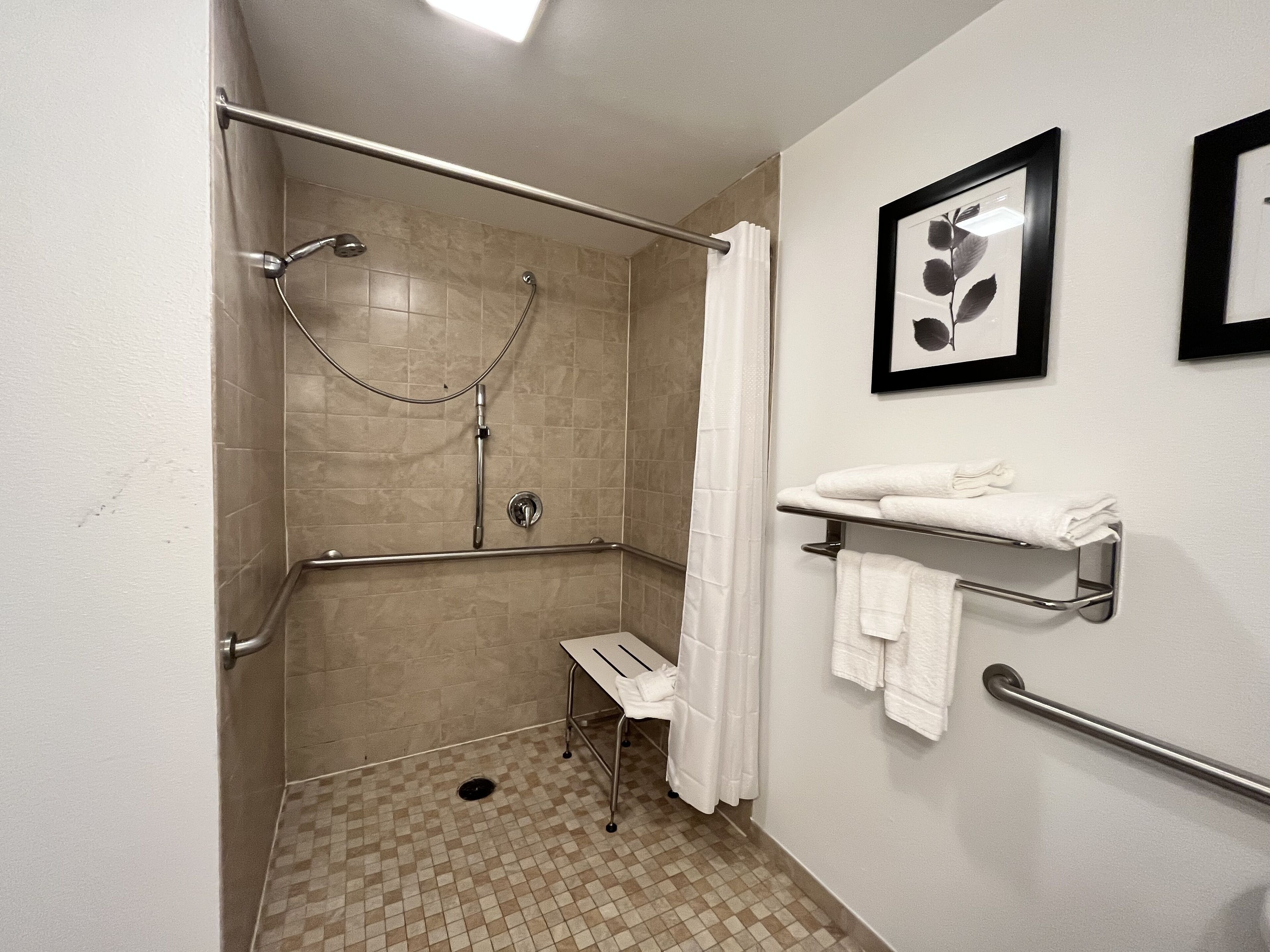A shower with a grab bar, a small step stool, and a towel rack with towels.