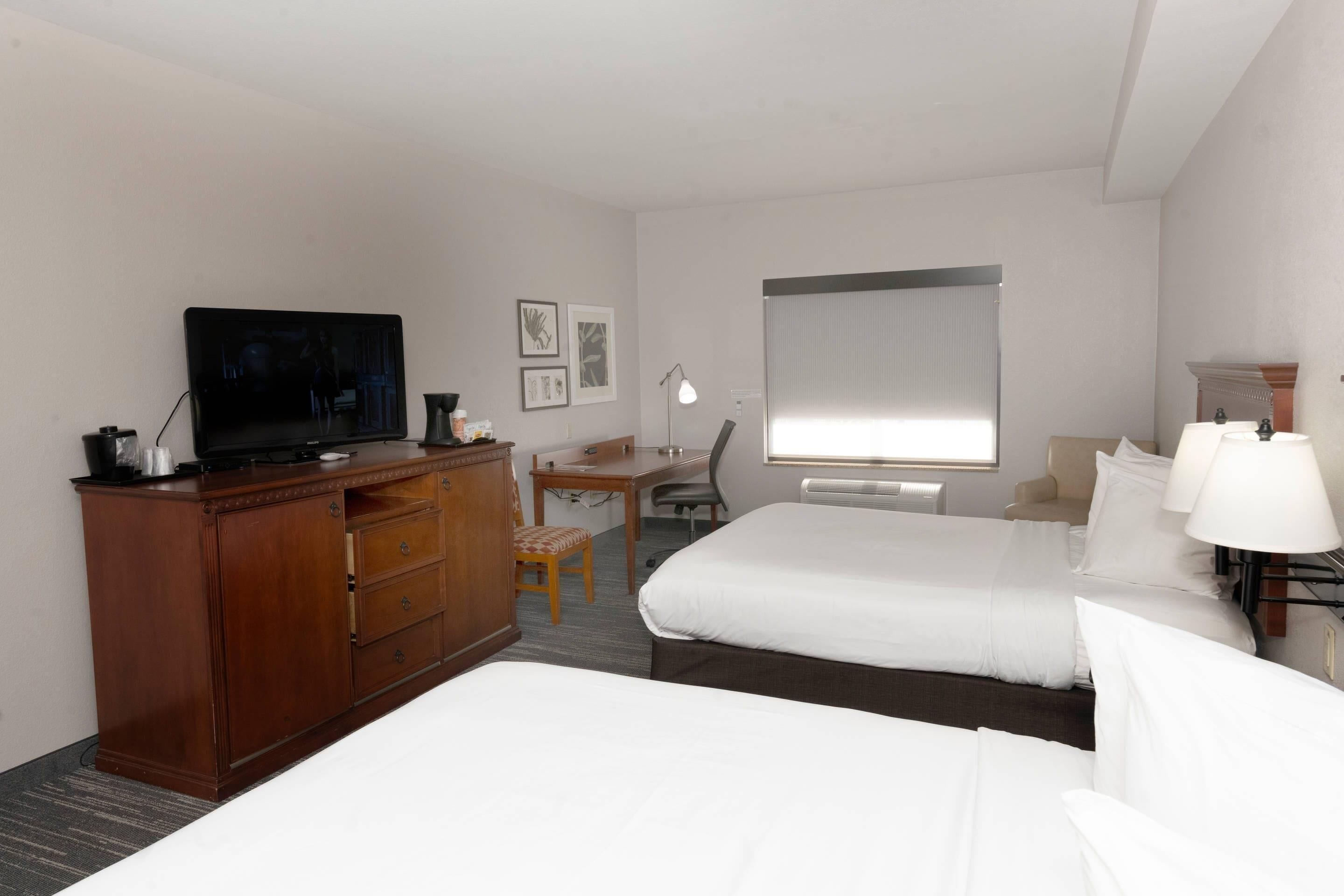 A hotel room with two beds, a desk, a television, a chair, and a window.