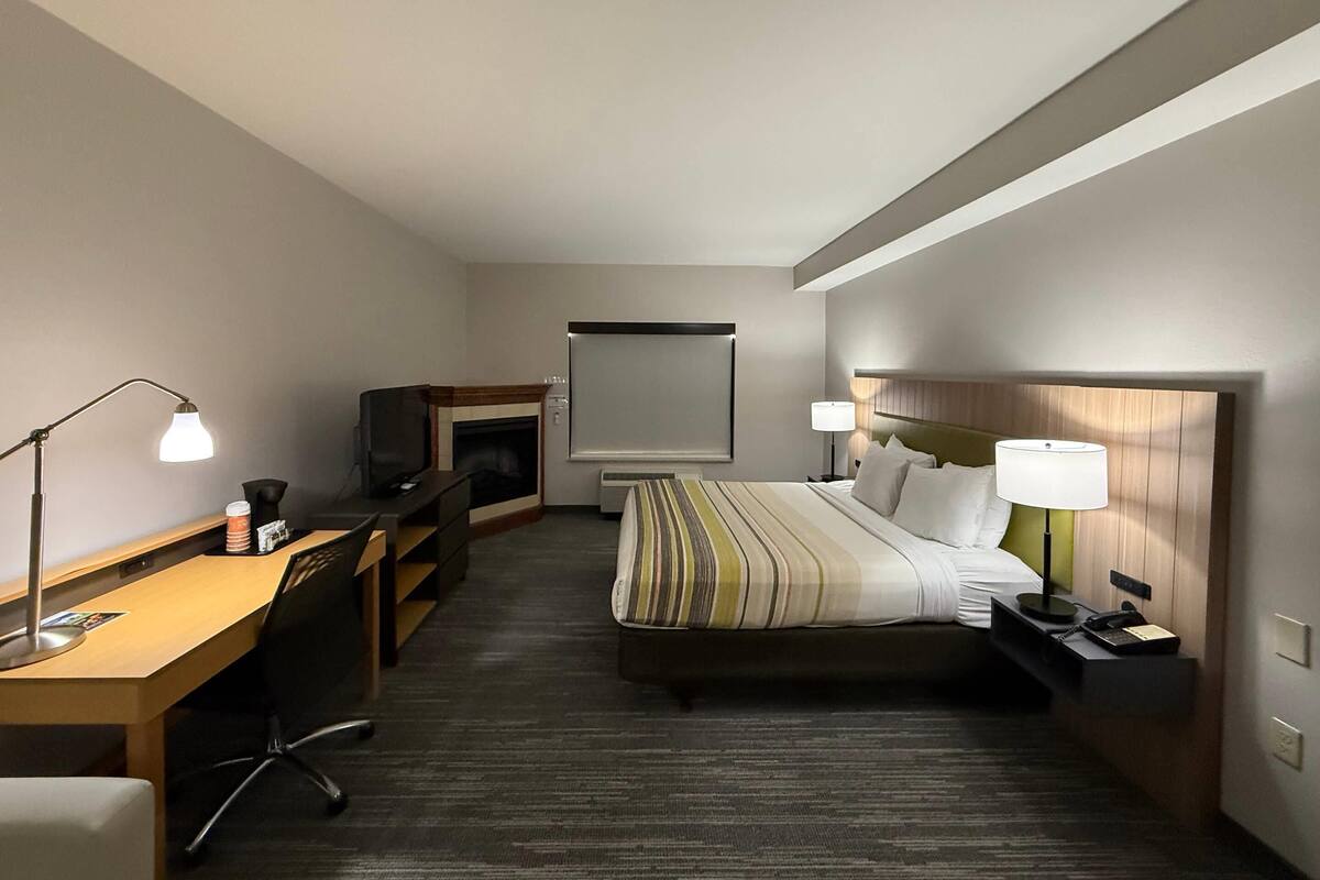 A hotel room with a bed, desk, chair, TV, and a fireplace.