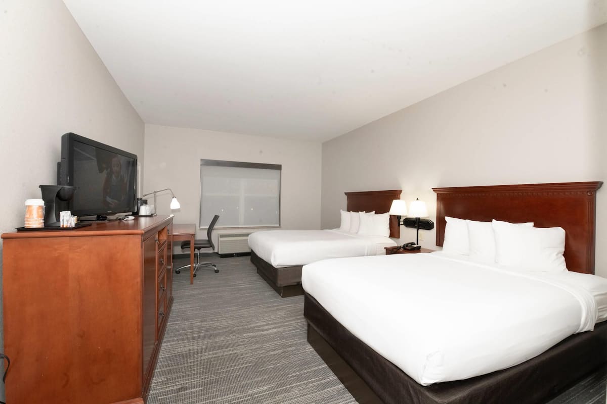 A hotel room with two beds, a desk, a television, and a window.