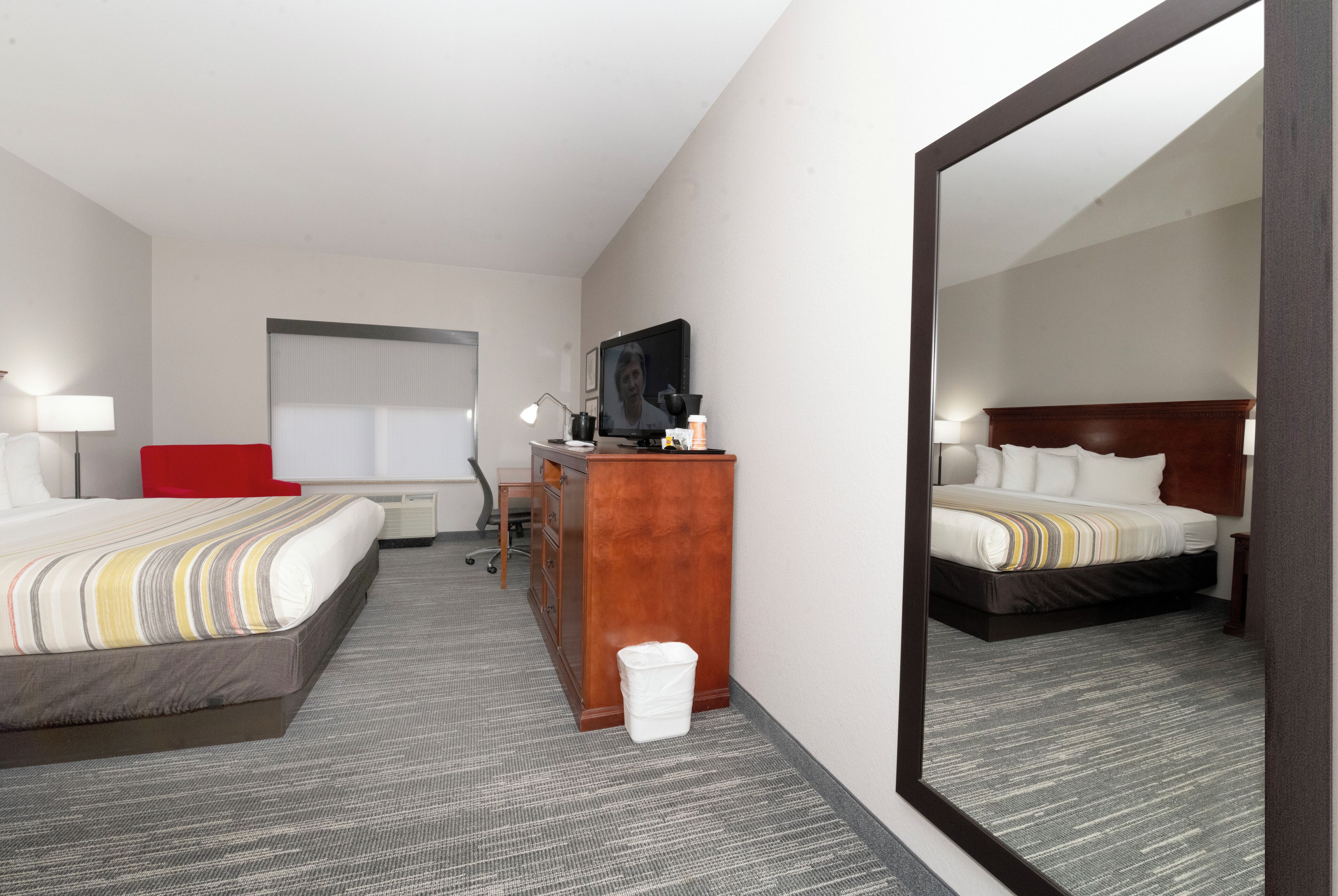 A hotel room with two beds, a desk, a chair, a TV, and a large mirror.