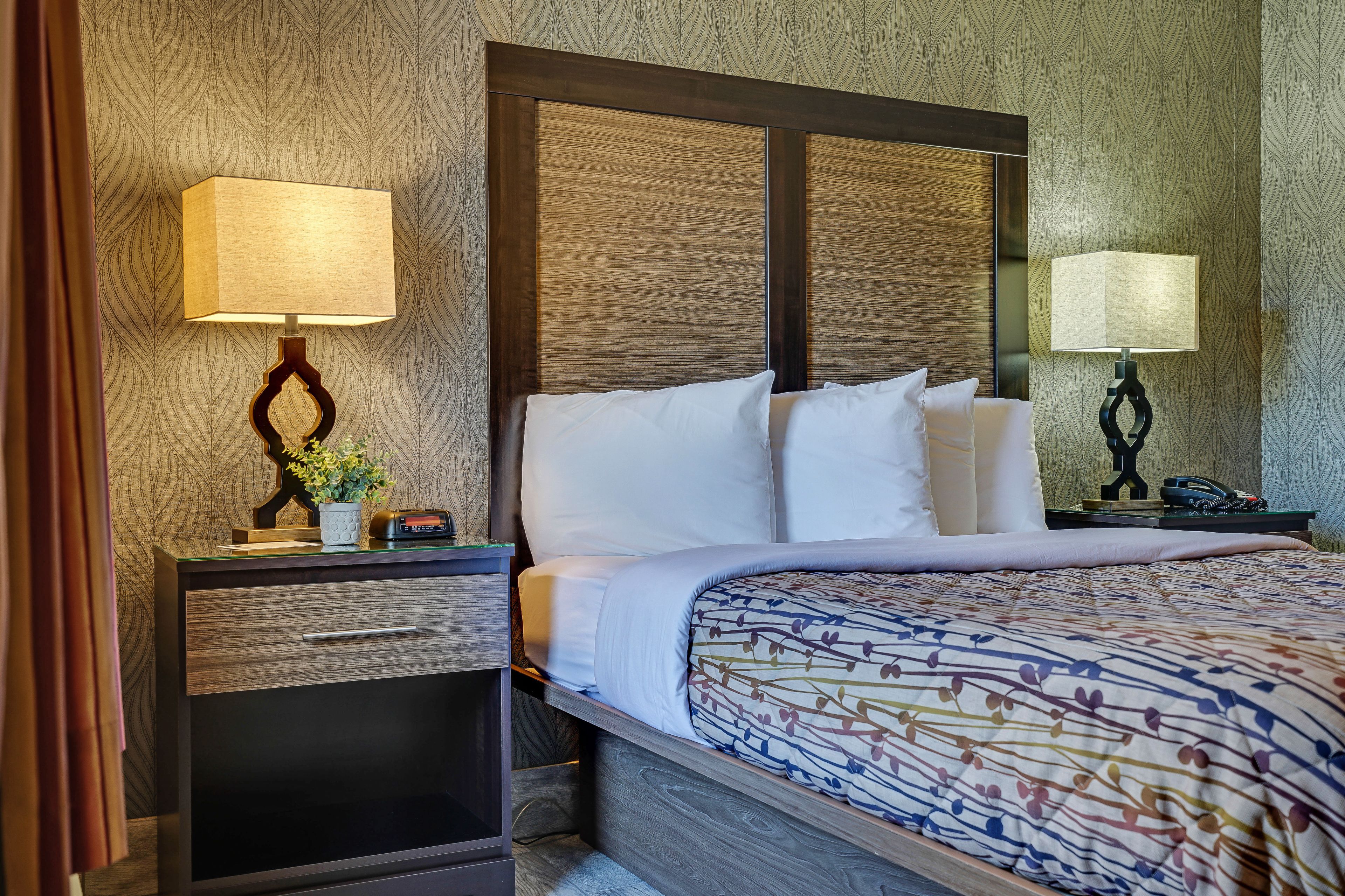 Una habitación de hotel con una cama, dos mesitas de noche, una lámpara y un espejo.
