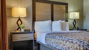 Una habitación de hotel con una cama, dos mesitas de noche, una lámpara y un espejo.