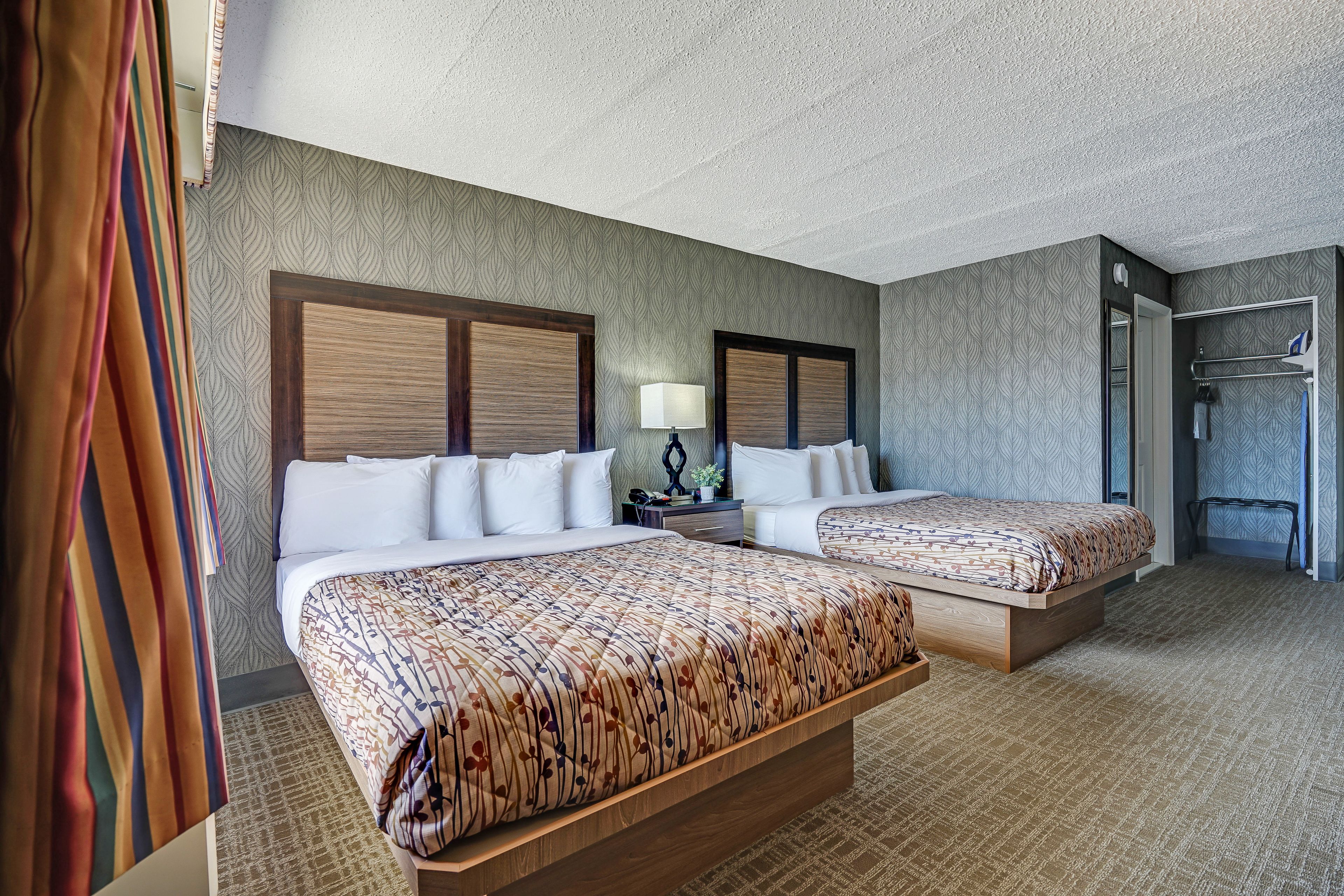 A hotel room with two beds, a nightstand, a lamp, and a shower area.