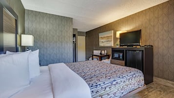 Quarto de hotel com uma cama grande, televisão, escrivaninha e área de estar.