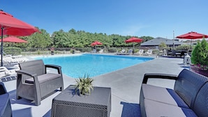 Un espace aménagé au bord de la piscine, avec des chaises longues, des parasols rouges et une piscine à l’eau d’un bleu limpide.