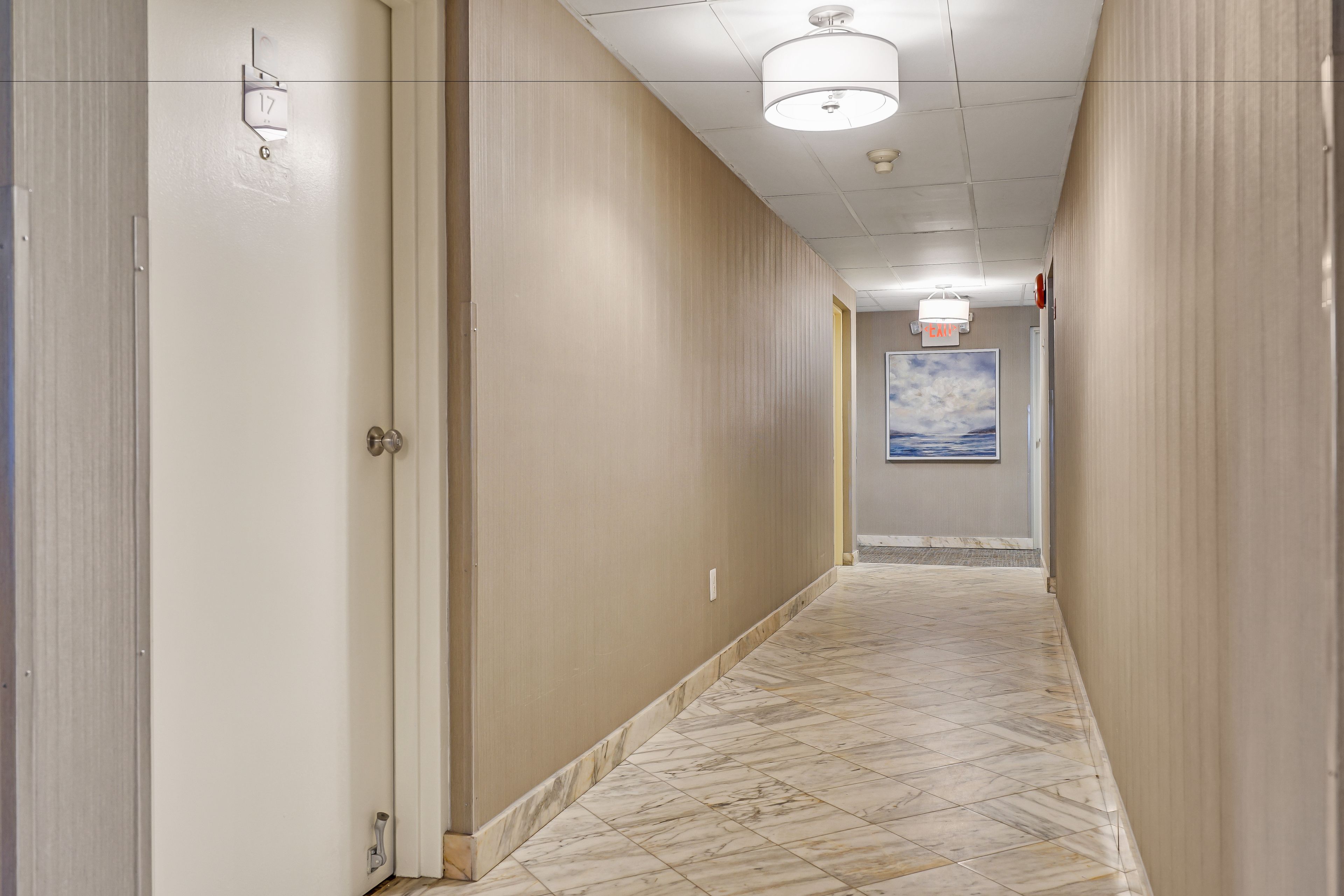A hotel hallway with a marble floor, beige walls, and a ceiling with recessed lighting.
