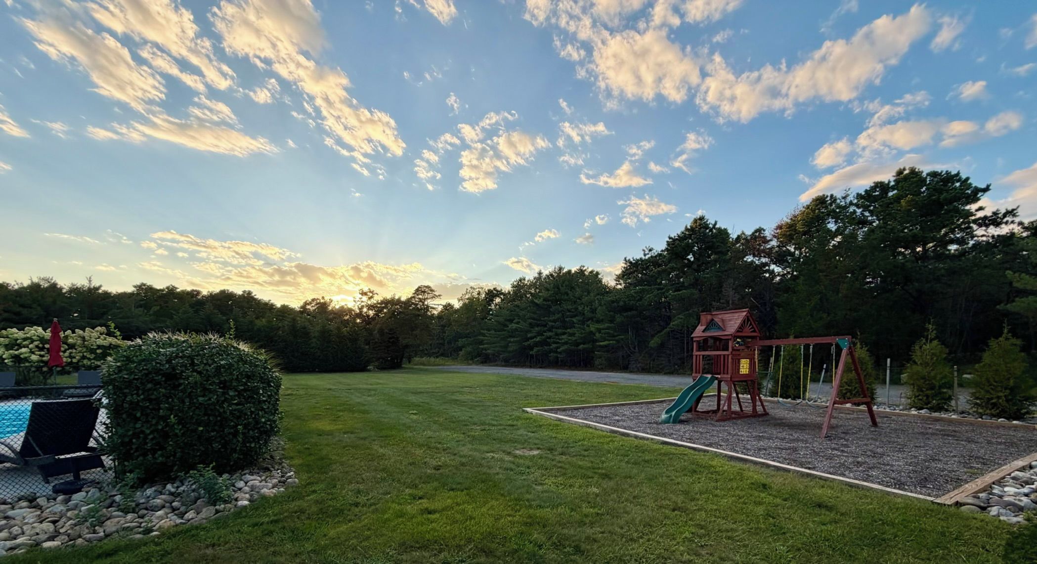 A backyard with a swing set, a slide, and a pool area.