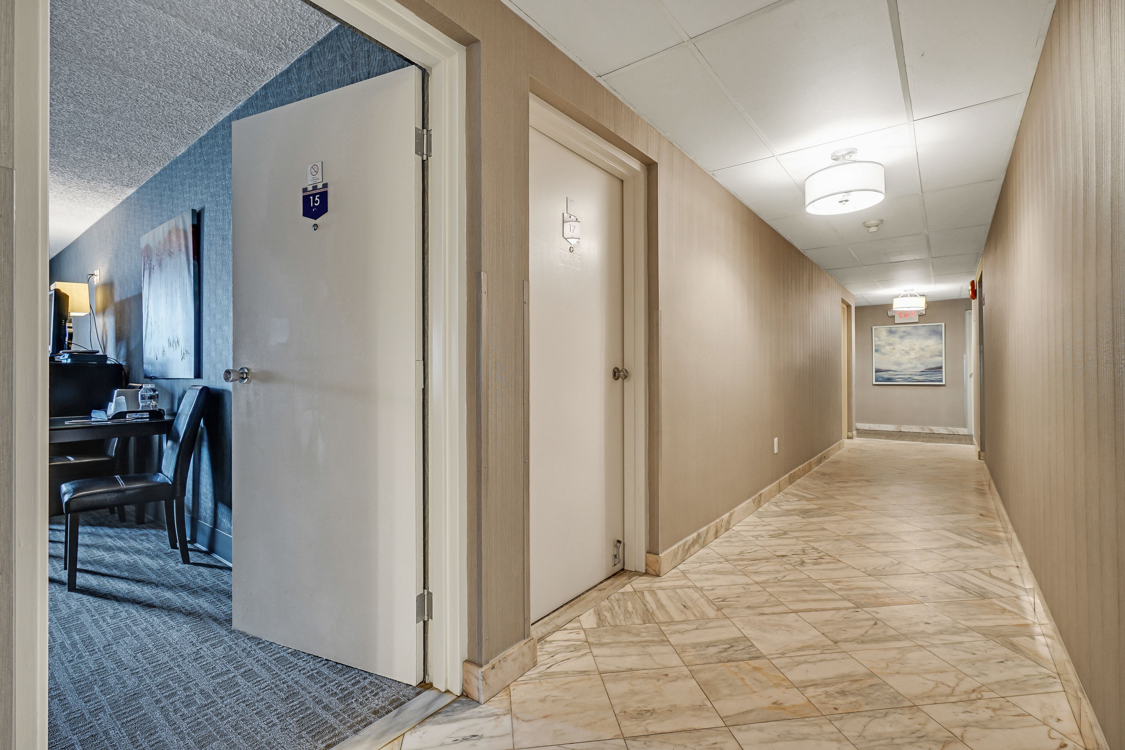 Een hotelgang met een tapijtvloer, een bureau met een stoel, en een deur met het nummer 15.