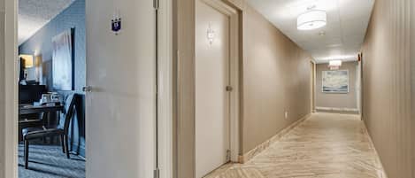 A hotel hallway with a carpeted area, a desk with a chair, and a door marked with the number 15.