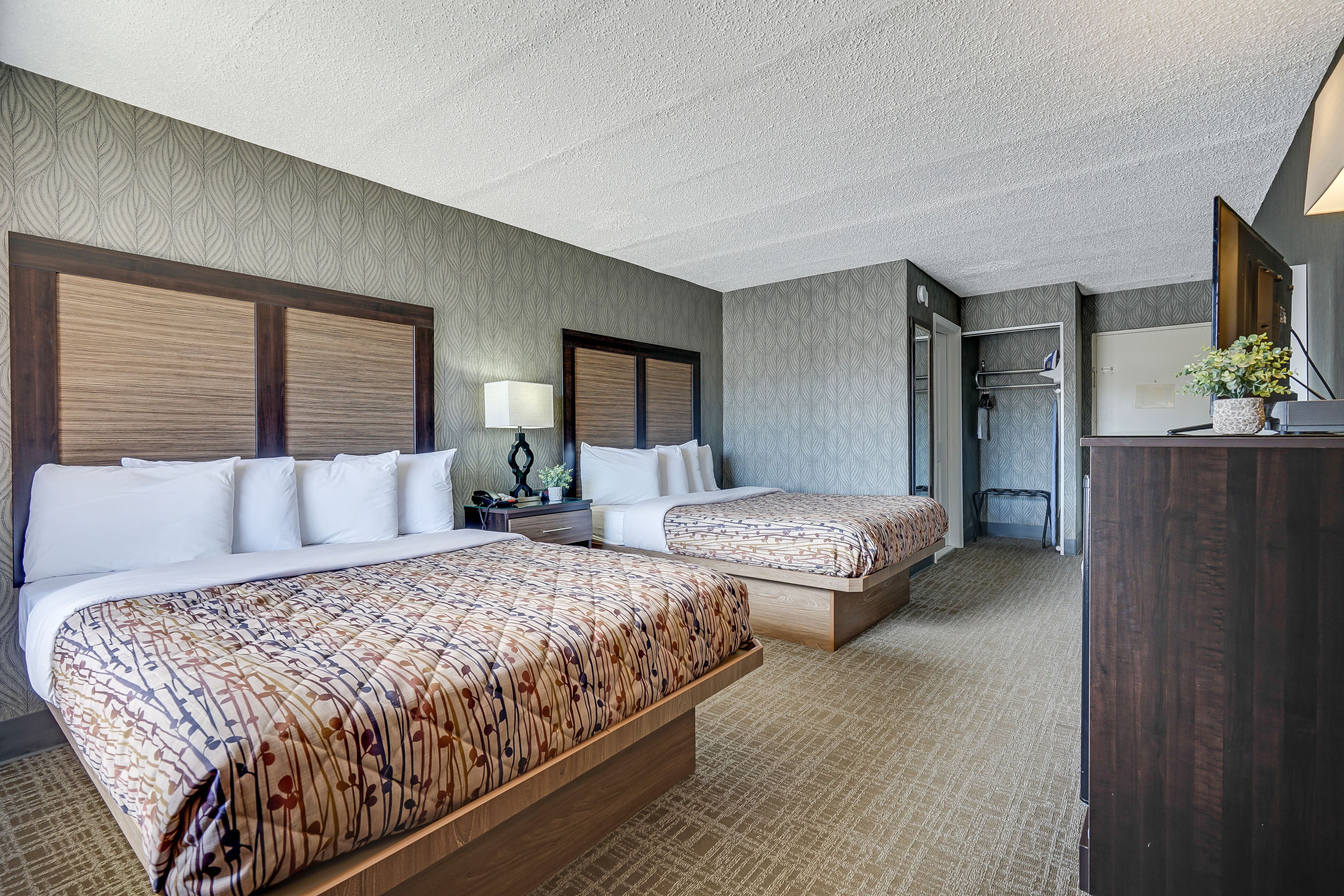 A hotel room with two beds, a desk, a lamp, and a shower area.