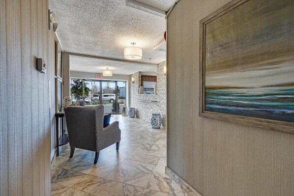 A hotel lobby with a marble floor, a gray armchair, a painting, and a stone wall.