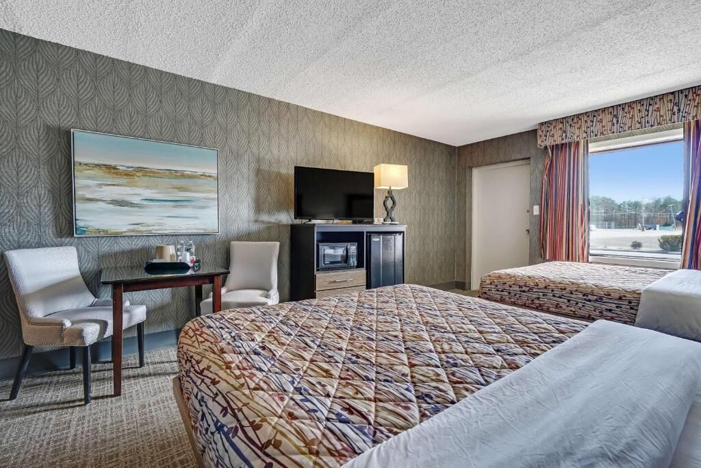 A hotel room with two beds, a desk with a television, a chair, and a window with curtains.