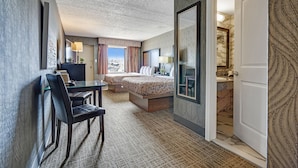 Une chambre d’hôtel avec un lit, un bureau et une chaise. On peut apercevoir la salle de bain à travers une porte ouverte.