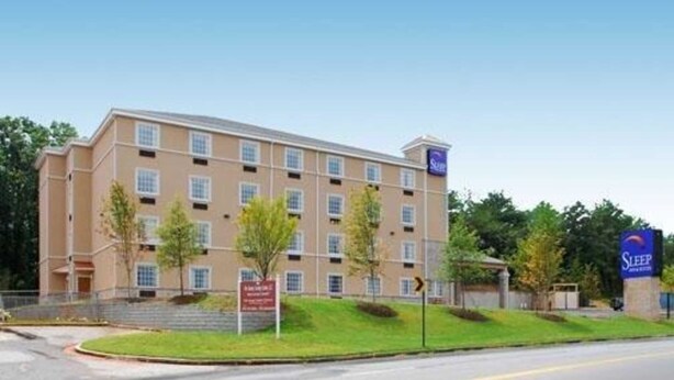 A multi-story hotel with a beige exterior, a sign indicating it is a Sleep Inn Express, and a clear blue sky in the background. - Sleep Inn and Suites at Kennesaw State University (Kennesaw)