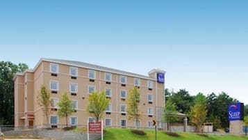 Een meerhoog hotel met een beige gevel, een bord waarop staat Sleep Inn Express, en een helderblauwe lucht op de achtergrond.